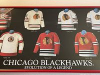 Close-up of several Chicago Blackhawks historical jerseys including 1957-58, 1962-63, 1965-66, 1972-73 models with their logos and colors visible in a framed display, promoting the Evolution of a Legend series.