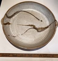 Top-down view showing the full circular plate/platter with abstract brown brushstroke pattern, showing overall glazed surface colors and texture.