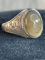 Close-up image of sterling silver ring with off-white cabochon stone showing bubbles inside and floral etched design on the band side.