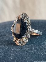 Close-up view of the sterling silver ring with large black faceted onyx center stone and marcasite stones set around it, lying flat on a dark surface.