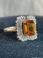 Close-up of the ring showing the brown emerald-cut stone surrounded by clear accent stones, highlighting one missing clear stone.