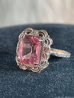 Close-up front view of sterling silver ring with large rectangular pink faceted stone and scalloped bezel setting.
