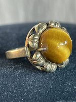 Close-up view of the sterling silver gold filled ring with round tiger eye stone on a dark fabric background showing the setting detail