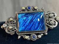 Close-up of front of Victorian butterfly wing brooch showing rectangular iridescent blue butterfly wing and ornate silver-tone frame with blue and clear accent stones.