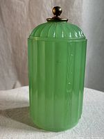 Front view of the jadeite glass container with brass finial lid, showing overall shape and color.