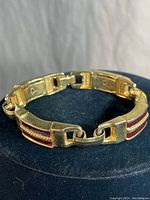 Full view of gold tone bracelet with red glass panels and chain accent design, laid circular with background