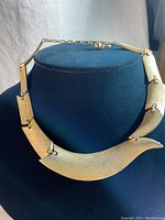 Photo showing the full choker necklace on a black display, highlighting the linked curved gold tone plates with a textured finish.