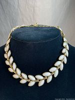 Full view of vintage Triffari choker necklace on a black display stand, showing gold tone metal and white poured glass leaf shapes.