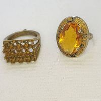 Photo showing two rings side by side: one with a large oval citrine gemstone and one with multiple smaller yellow stones in an openwork setting.