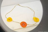 Photo showing full necklace with three glass beads in orange and yellow on a gold-filled thin chain.