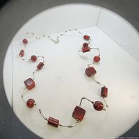Full view of handmade vintage red bead necklace with silver links laid out on white background.