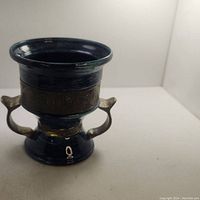 Photo showing the vintage metal vase with dark blue enamel and ornate metal band with handles on a white background