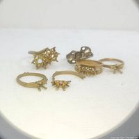 Photo showing six unfinished gold-tone ring settings in various styles with prong mounts for stones. Rings uncleaned and unpolished.