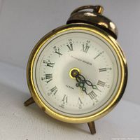 Close-up of the front of the Phinney Walker brass mechanical alarm clock with white dial showing Roman numerals and black hands with luminous tips.