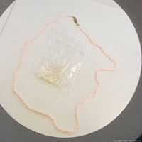 Pink rice pearl necklace strand laid out with small plastic bag of loose pearls on a flat white surface