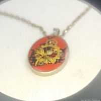 Close-up photo of silver 925 round resin pendant necklace featuring gold-tone butterfly and embedded gears on red background.