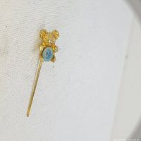 Close-up photo of gold-tone koala-shaped stick pin with oval black opal triplet gemstone.