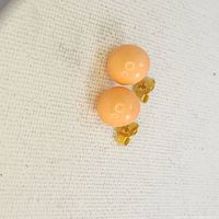 Photo showing two round coral button earrings with gold posts and backs on a textured white surface
