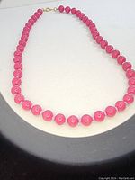 Hot pink round bead necklace arranged in a circle on a light surface, showing shiny polished beads and gold-tone clasp.
