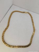 Full view of the vintage gold tone woven necklace laid flat on a white surface.