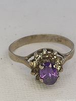 Close-up of the front side of the vintage ring showing an oval purple stone with multiple clear stones arranged asymmetrically around it. The metal band is plain with vintage wear.
