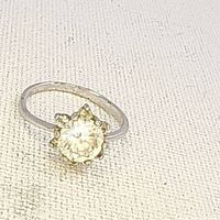 Close-up of vintage ring with clear round faceted stone in prong floral/starburst design and open band