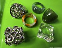 Overview of all six rings displayed on green background including steampunk gear ring, fidget ring and four resin rings in assorted colors.