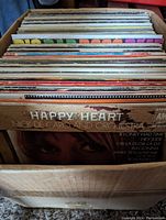 Box showing side view of assorted vinyl records with 'Happy Heart' album visible on top.