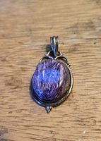 Front view of the oval purple stone pendant against a wooden background, showing the swirly pattern inside the stone and silver setting