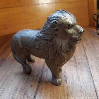 Front and side angle of the antique cast iron lion piggy bank showing details of the mane and coin slot on top.
