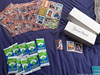 Two open white storage boxes containing two stacks of baseball cards, ten sealed pre-rookie packs displayed in front, loose cards shown in sleeves.