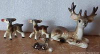 Set of four ceramic deer miniatures, showing adult stag and three fawns arranged together on surface with neutral background