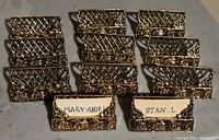 Front view of the eleven gold tone metal place holders arranged in rows with some containing handwritten name cards.