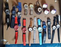 Full view of the lot showing 16 watches with various strap materials and colors laid out on cardboard.