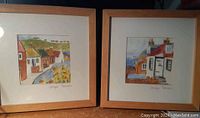 Pair of framed watercolor prints displayed side by side on a tabletop