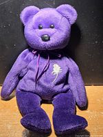 Front view of purple Ty Princess Diana Beanie Baby showing plush fabric, facial details, ribbon and embroidered rose on chest.