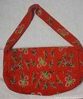 Front view of a red purse covered in floral beadwork with beaded strap.