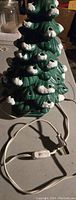 Front view of vintage green ceramic Christmas tree with white snow accents and power cord on table.