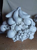 Full frontal view of the white porcelain cornucopia fruit bowl centerpiece showing sculpted bananas, grapes, apples, and cherries detail.