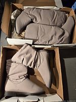 Two pairs of beige boots in boxes, one pair taller than the other, shown from top angle