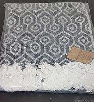Packaged grey and white geometric patterned cotton throw with fringe detail.