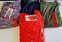 Four new Buffalo David Bitton ladies long sleeve knit tops laid out showing various colors and patterns, each size medium with tags/stickers