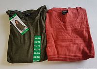 Two long sleeve knit tops, one olive green with tags and one coral with textured patterns, laid side by side on white surface