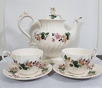 Five-piece white ceramic tea set with floral and leaf pattern, teapot, two cups, two saucers shown from front