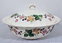 Side view of white ceramic covered serving bowl showing multicolor floral and berry decorative pattern and scalloped edges.