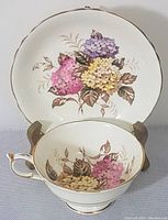 Close view of tea cup and saucer with floral lilac pattern and gold trim shown on wooden display stand.