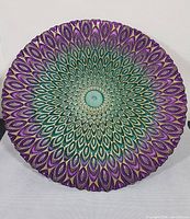 Top view showing full peacock feather pattern in iridescent purples, greens, and blues on round plate with scalloped edges.