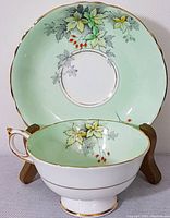 Photo showing tea cup and saucer facing forward displaying the detailed floral pattern and gold trim on pale green background.