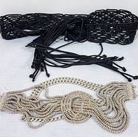 Photo showing the black open weave knit cotton belt with long tasseled fringes next to the silver tone metallic chain belt with textured thick links.