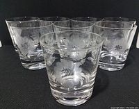 Eight clear blown glass old fashioned glasses featuring etched cornflower floral pattern displayed with some glasses closer showing details.